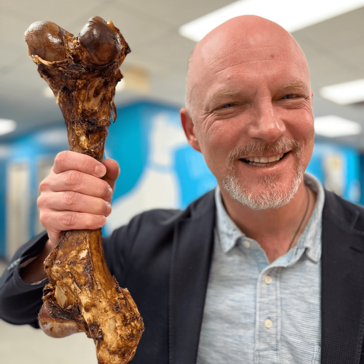 A bald man holding up a Monster Femur Bone from Best Bully Sticks in a lab.